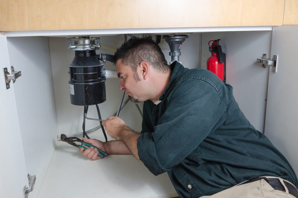 A plumber laying under a house hold sink working on a garbage disposal.