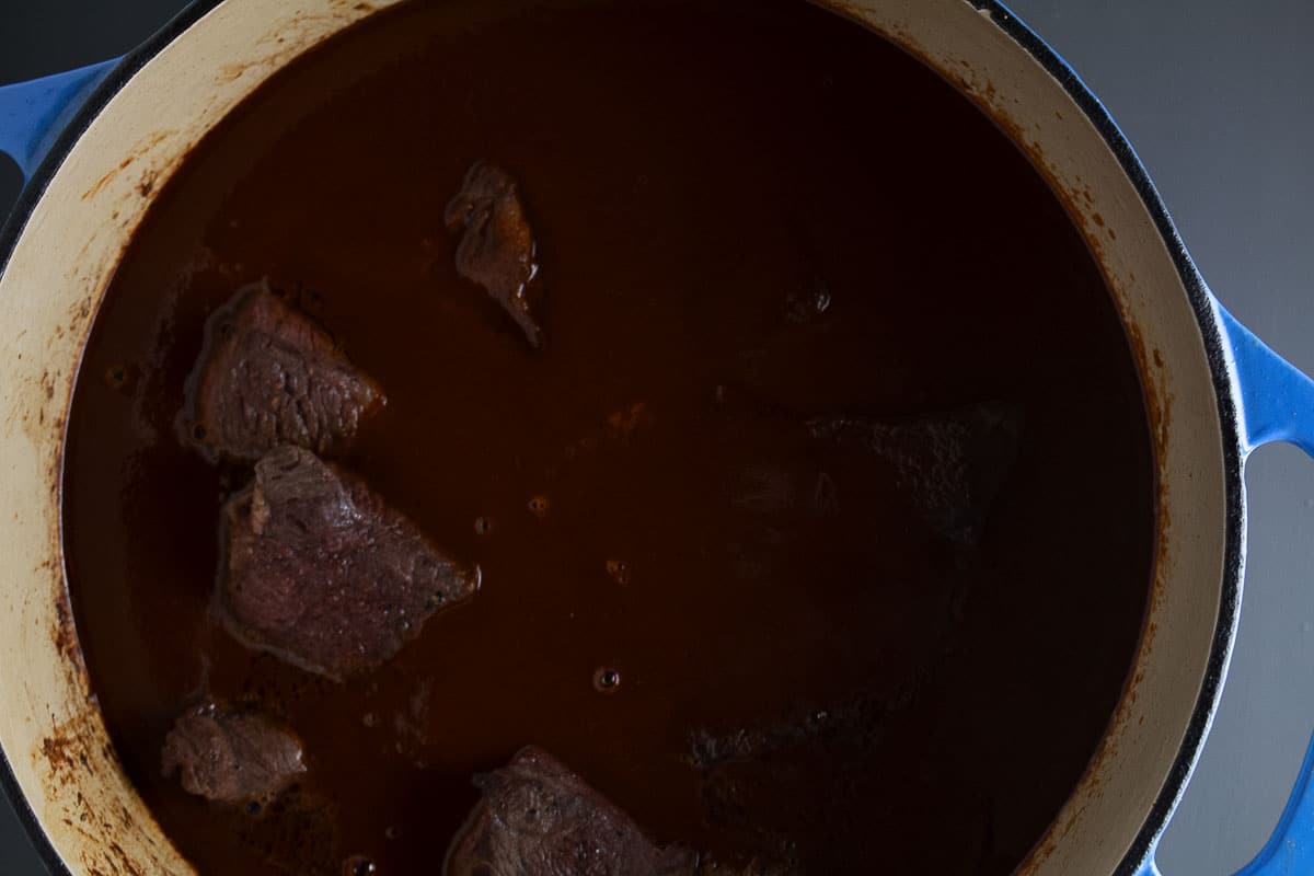 This image show the browned chuck roast in the dutch oven with the chile sauce.