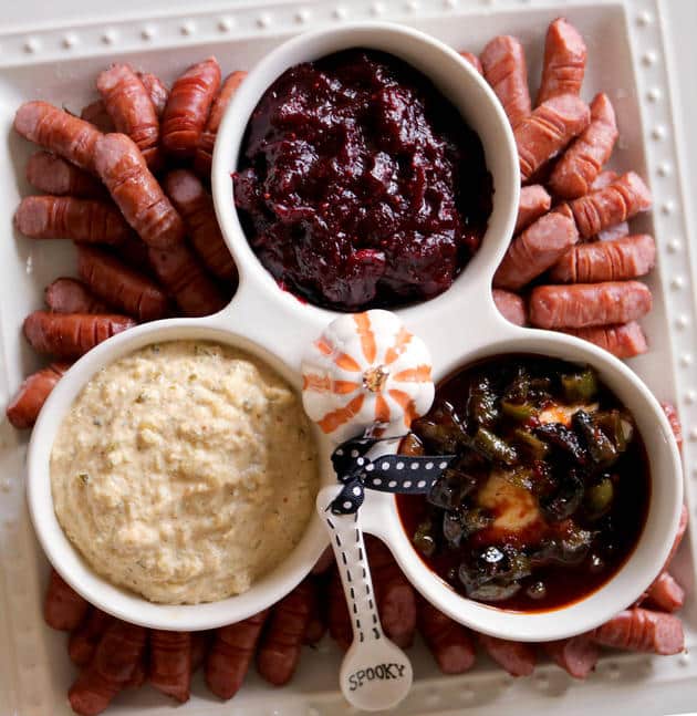 Little smokie fingers on white platter with three dipping sauces.