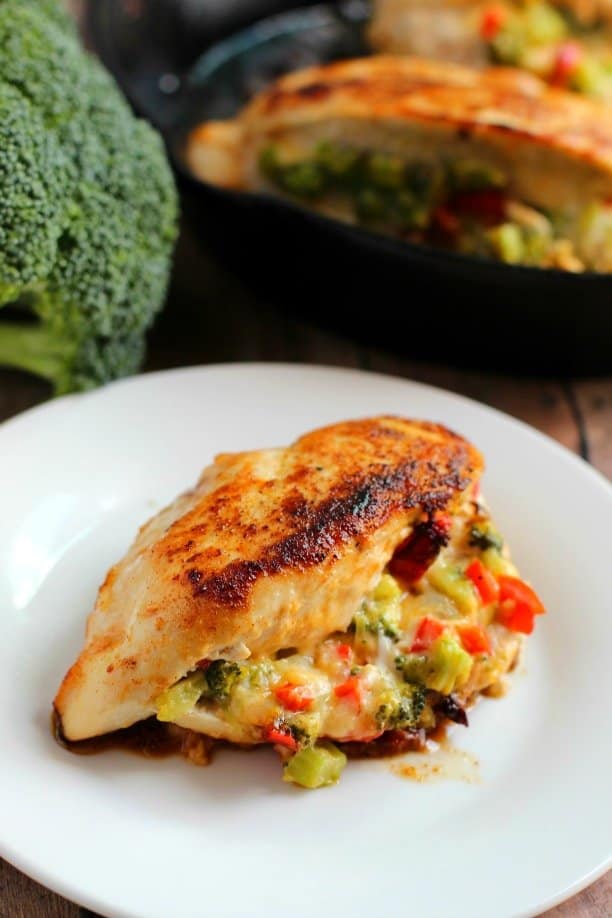 Low carb broccoli cheese stuffed chicken on white plate with broccoli in the background.