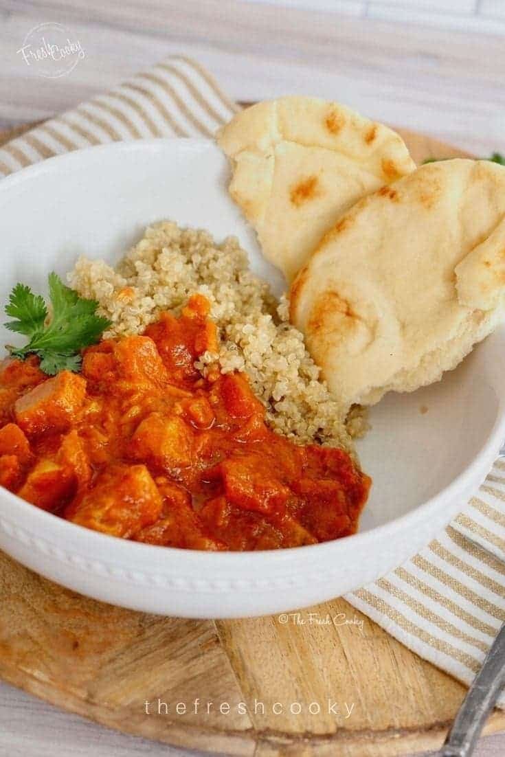 Coconut curry chicken over quinoa and bread in white bowl with napkin in background.