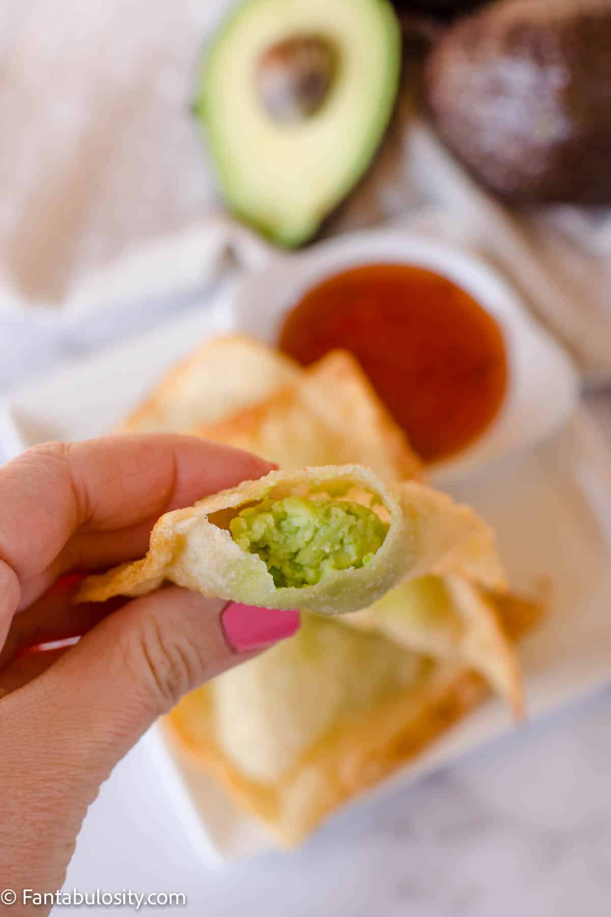 Avocado wonton in hand with more in background.