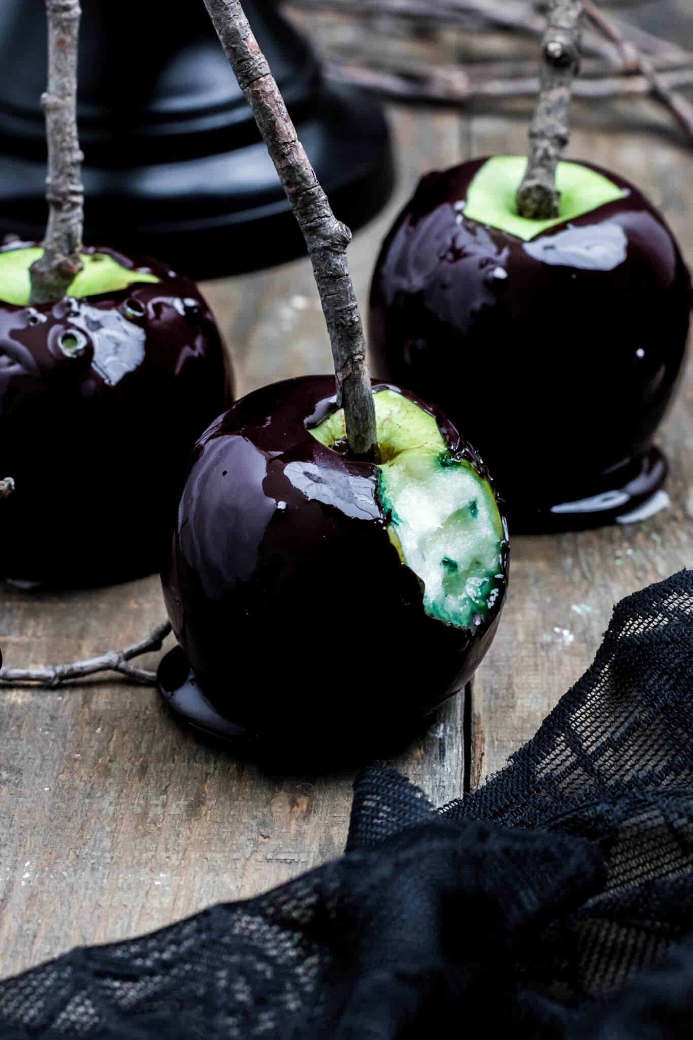 Very dark candy coating on green apples with natural wood stick on wooden background.