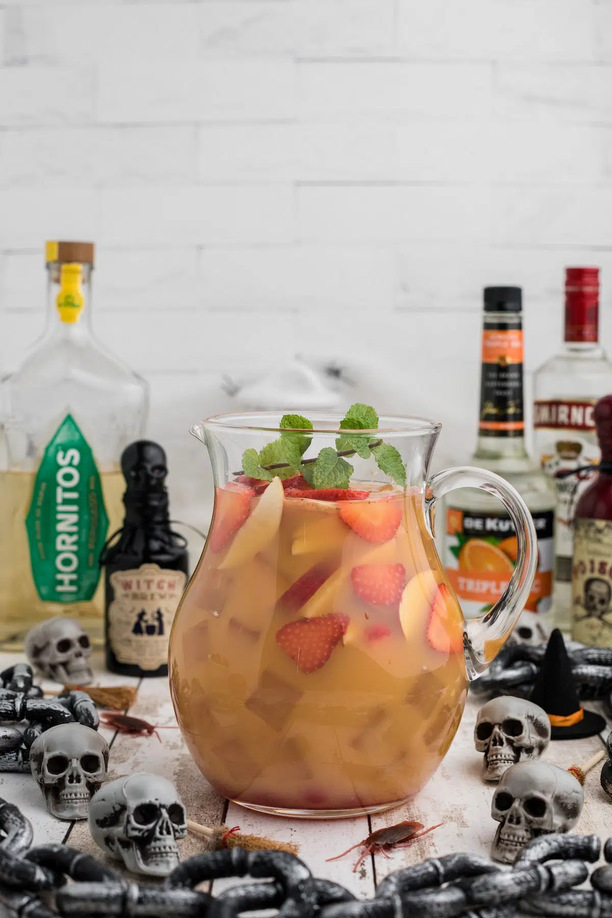 Chopped fruit with alcoholic beverage in pitcher with Halloween decorations and ingredients in the background.