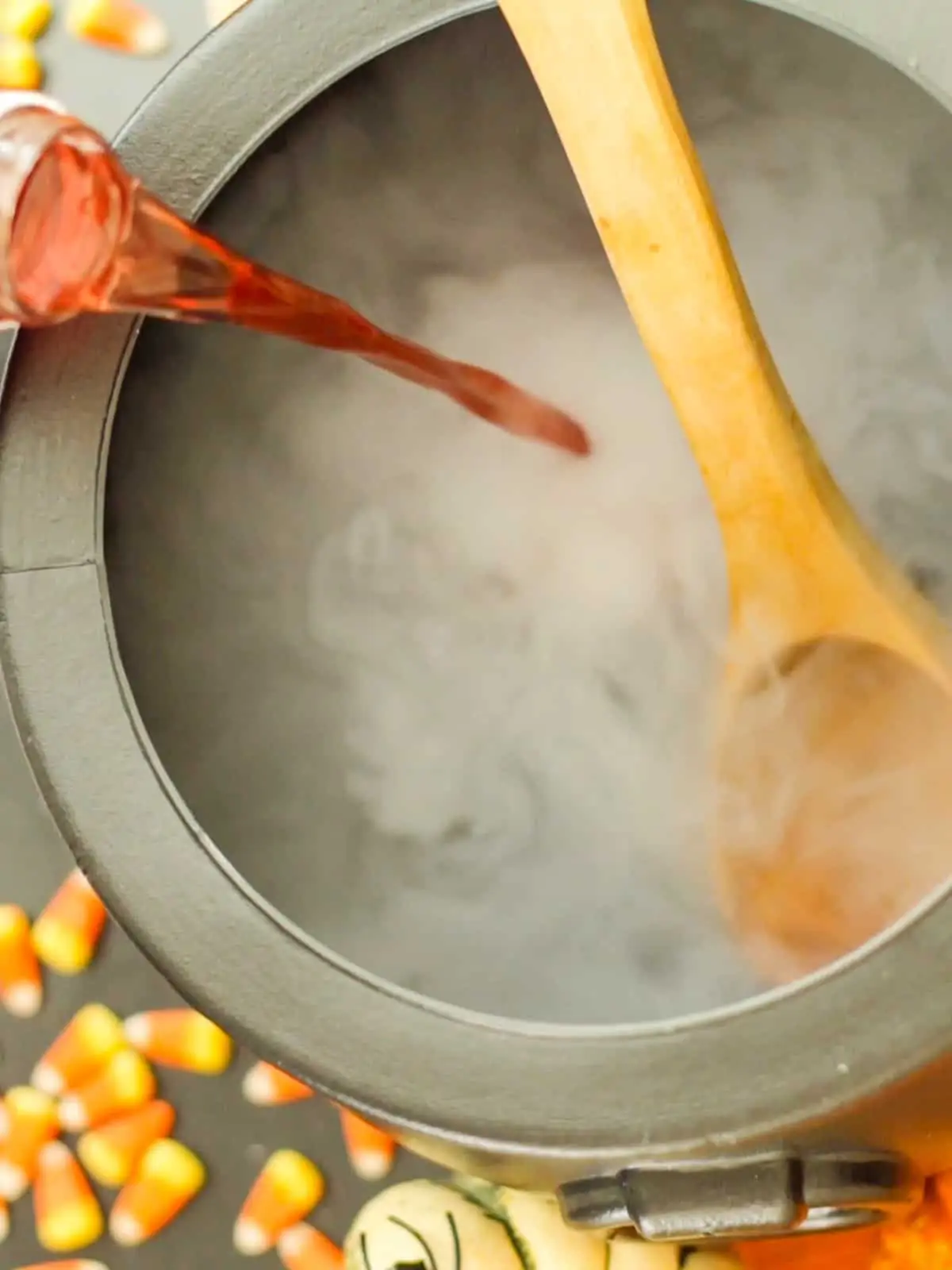 Toy cauldron with smoke emanating from it with candy corn in the background.