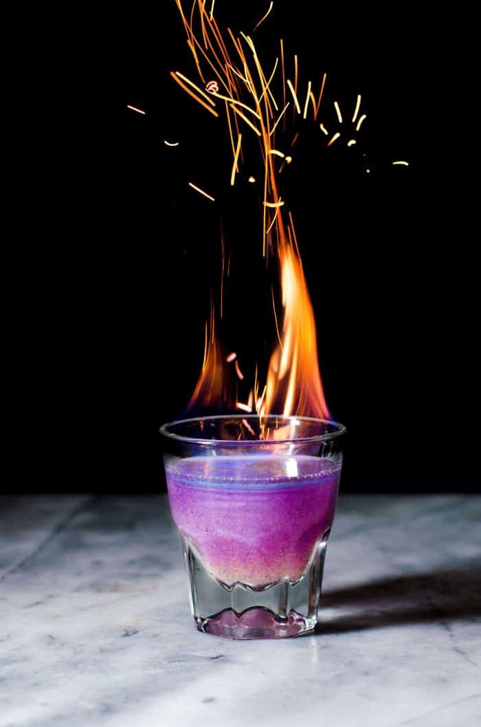 Purple Phoenix cocktail with fire and with dark background.