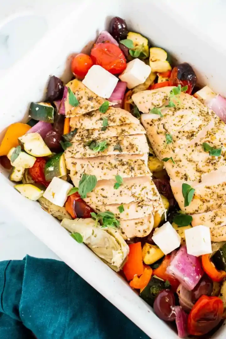 Sheet pan Greek chicken with colorful vegetables on a white plate with turquoise napkin.