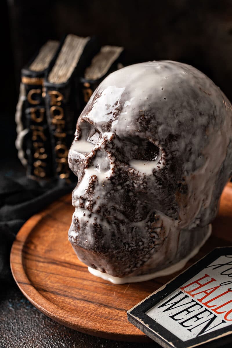 Cake in the shape of a skull with books in the background on top of a rotating tray.