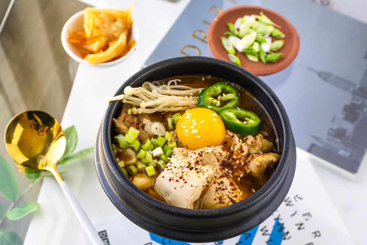 Soondubu (tofu soup) soup recipe in a bowl with garnishes on saucers.