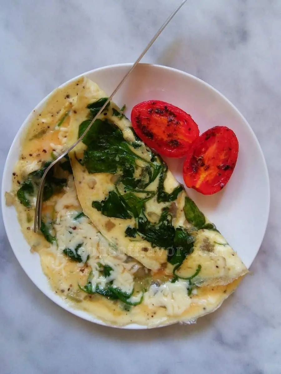 Omelet with spinach, cheese and tomato slices and fork on white plate.