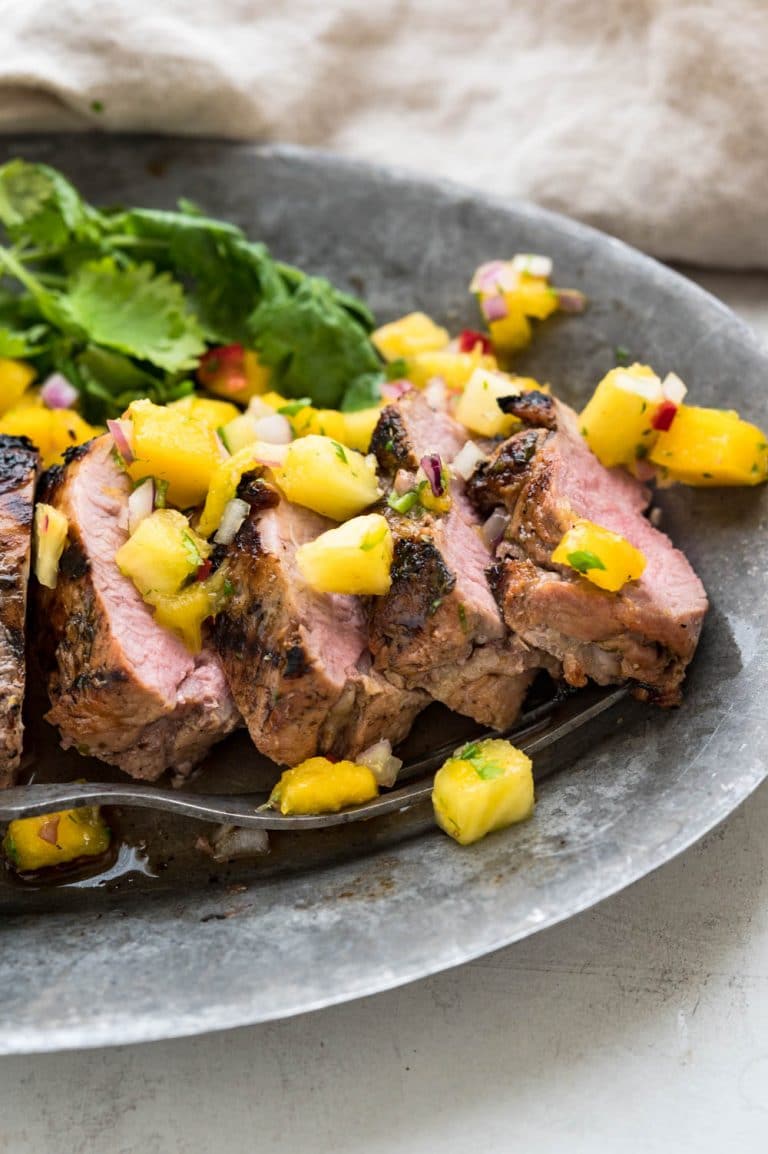 Tequila marinated pork with mango pineapple salsa on gray plate and fork.