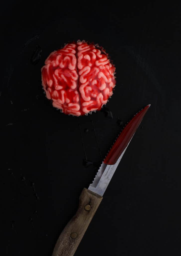 Cupcakes with frosting made to look like brains with corn syrup blood and knife on dark background.