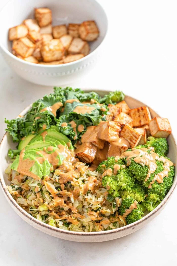 Tofu, broccoli, leafy green, vegan dinner bowl on white background.