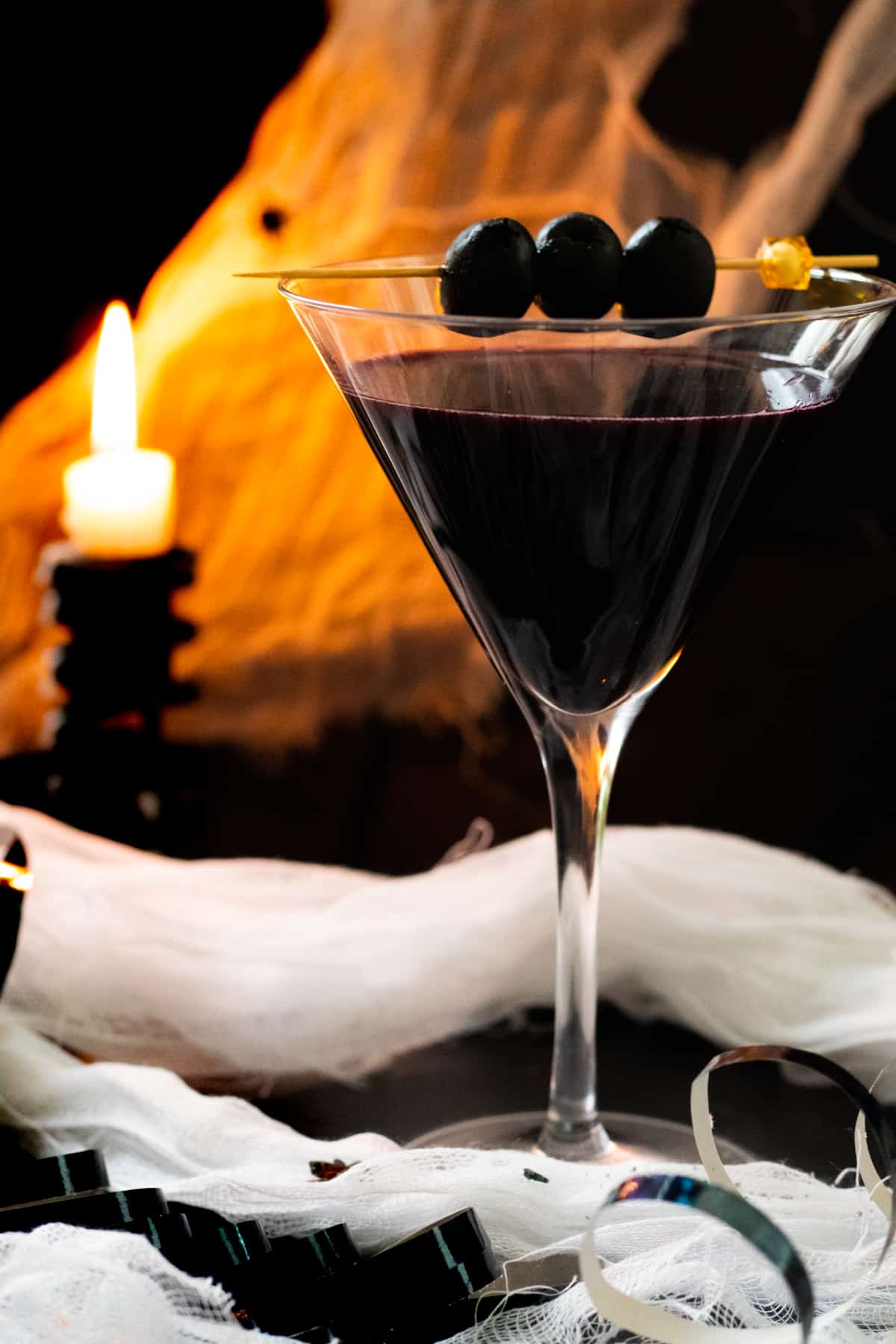 Dark colored martini in glass with fire in the background.
