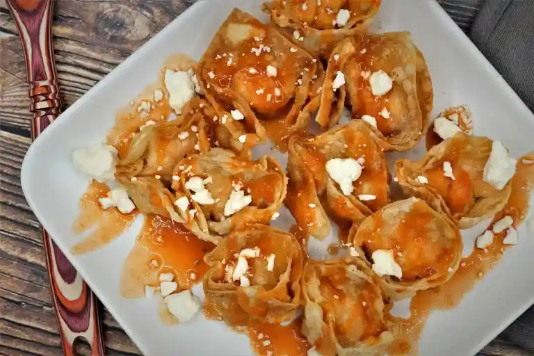 Crispy Buffalo Chicken wontons on white plate and wooden background.