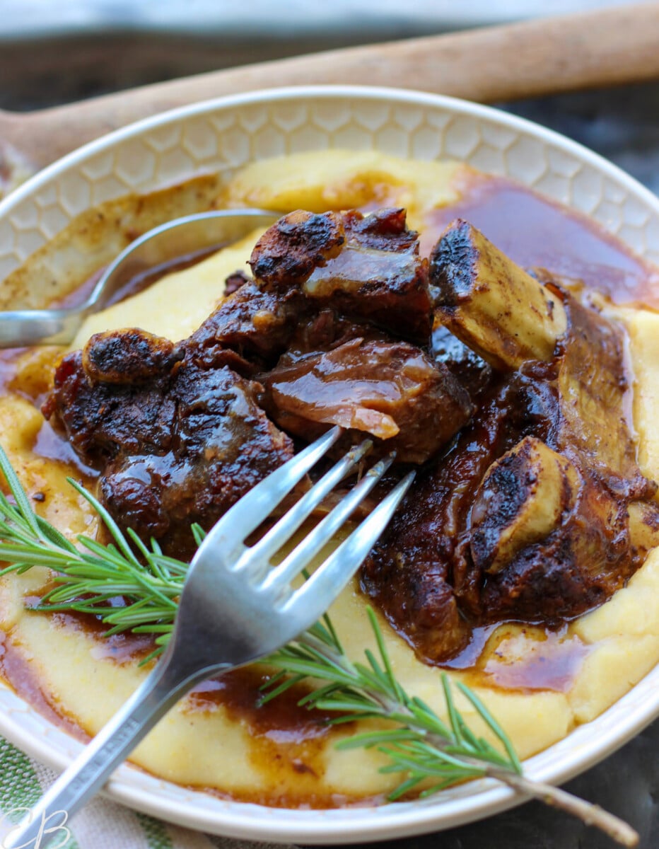 Beef short ribs and gravy served over cauliflower mash in white bowl with fork and spoon.