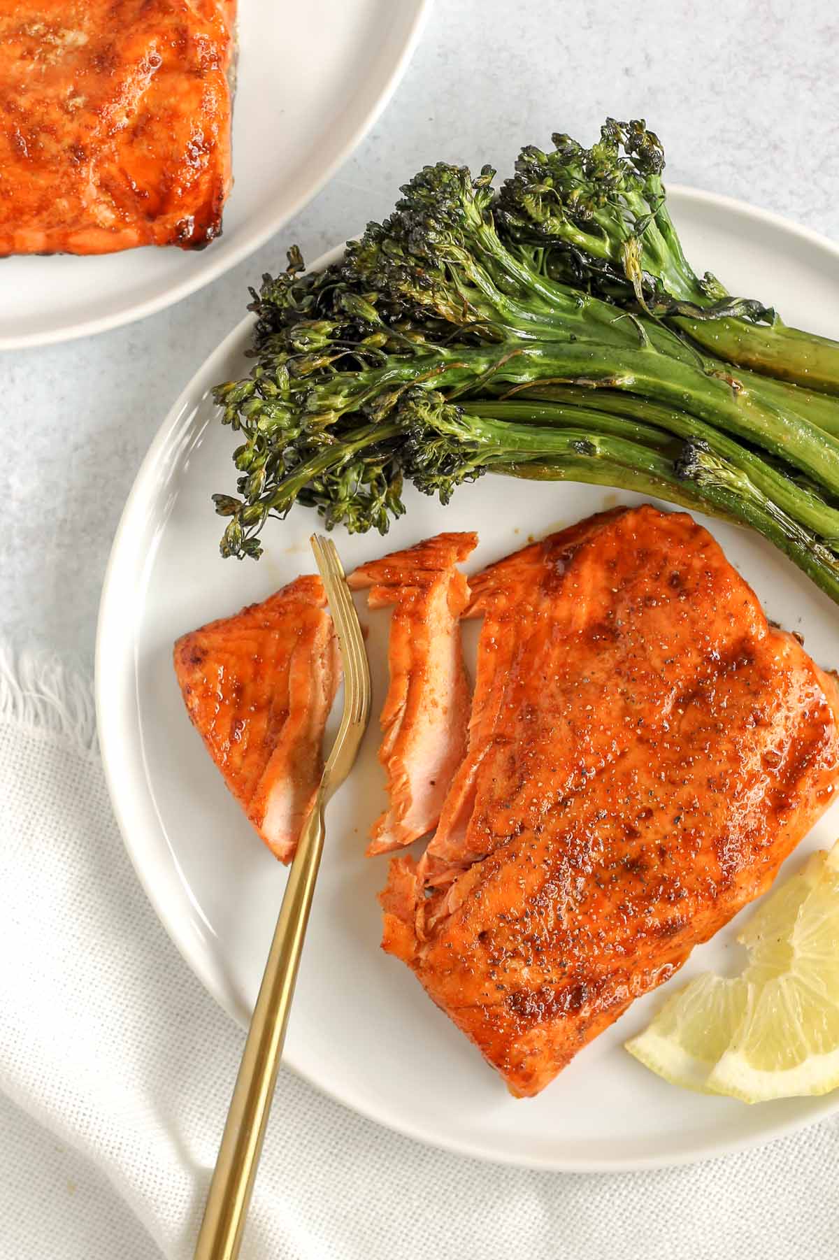 Air fryer frozen salmon with broccoli and lemon on white plate.