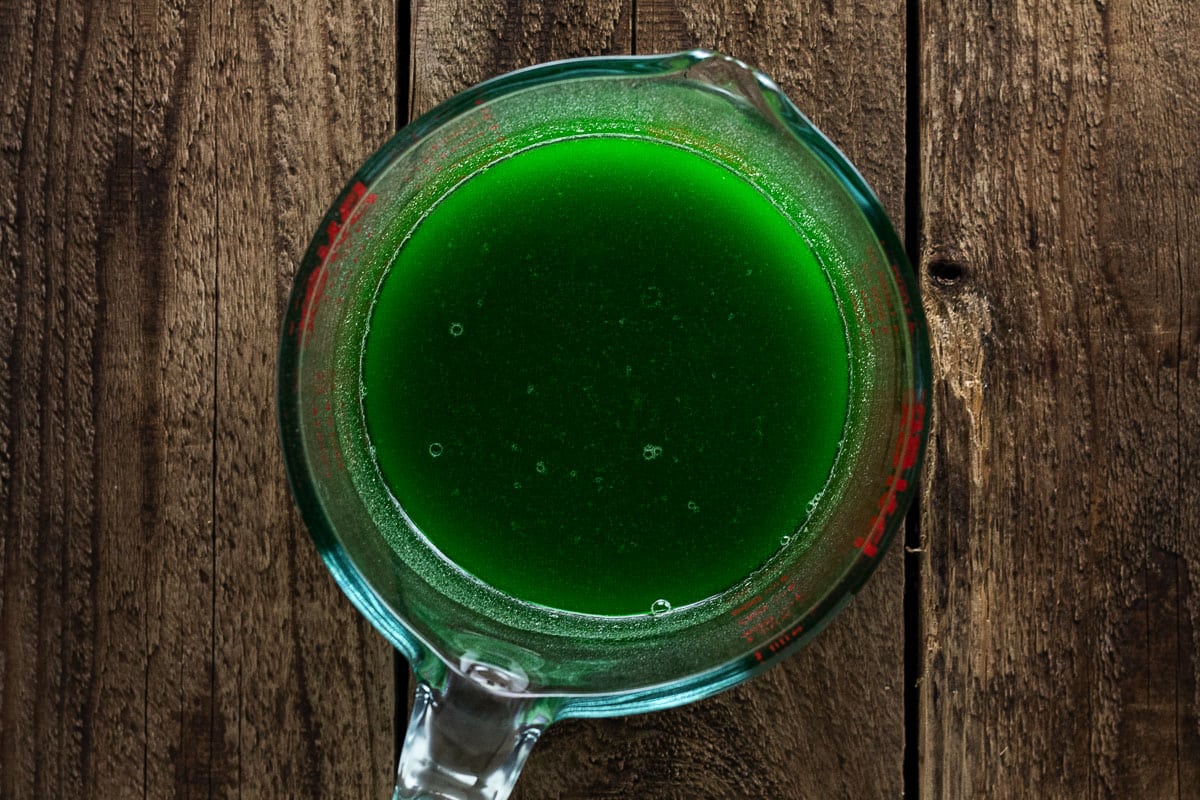 Green apple gelatin mixture in microwave save measuring cup on wooden background.