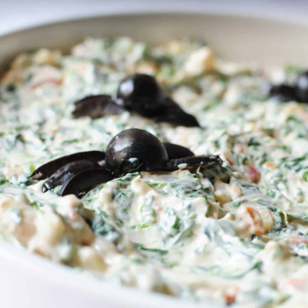 Halloween spinach dip with black olive spiders on top.