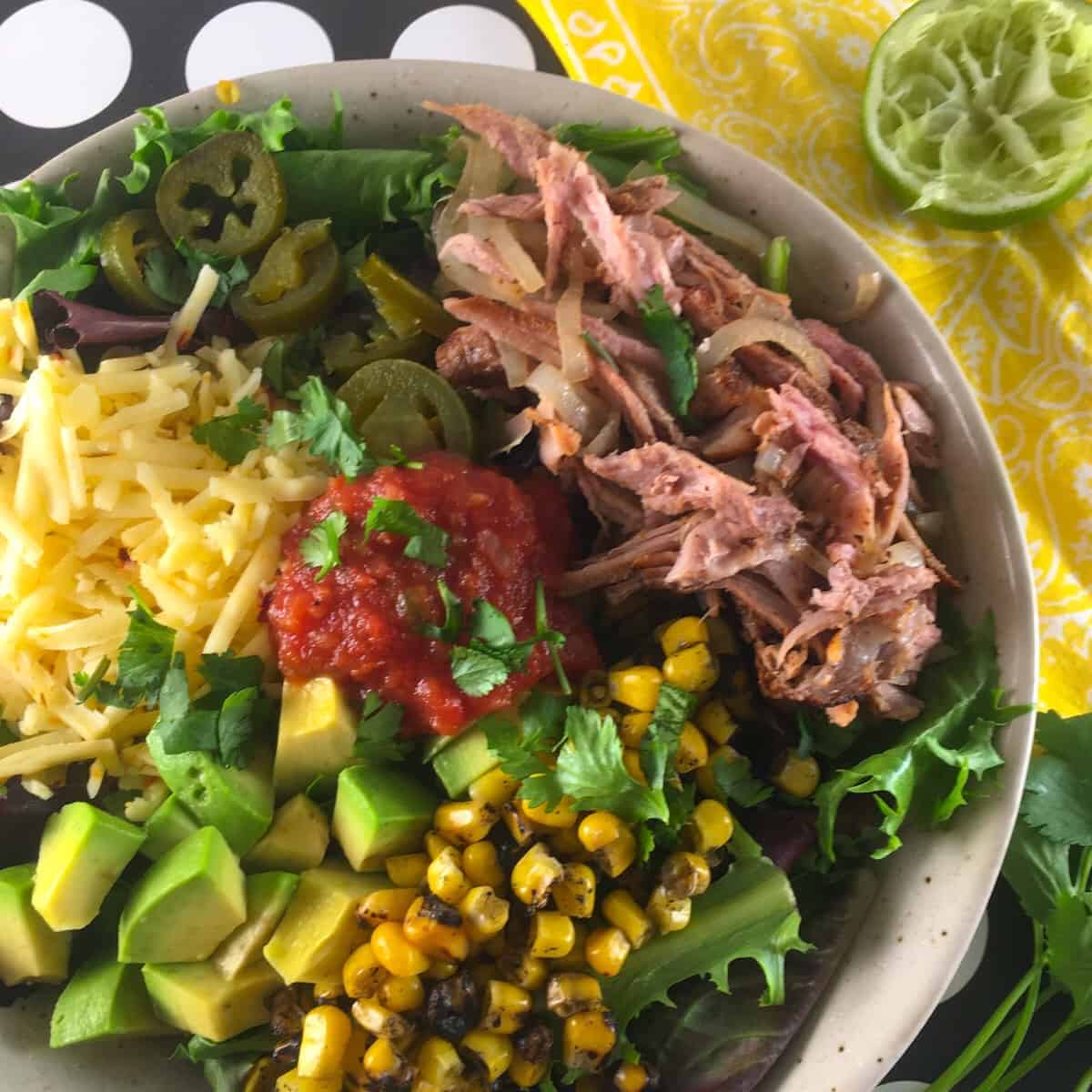 Pork, salsa, cheese, lettuce, corn, and avocado in a bowl.