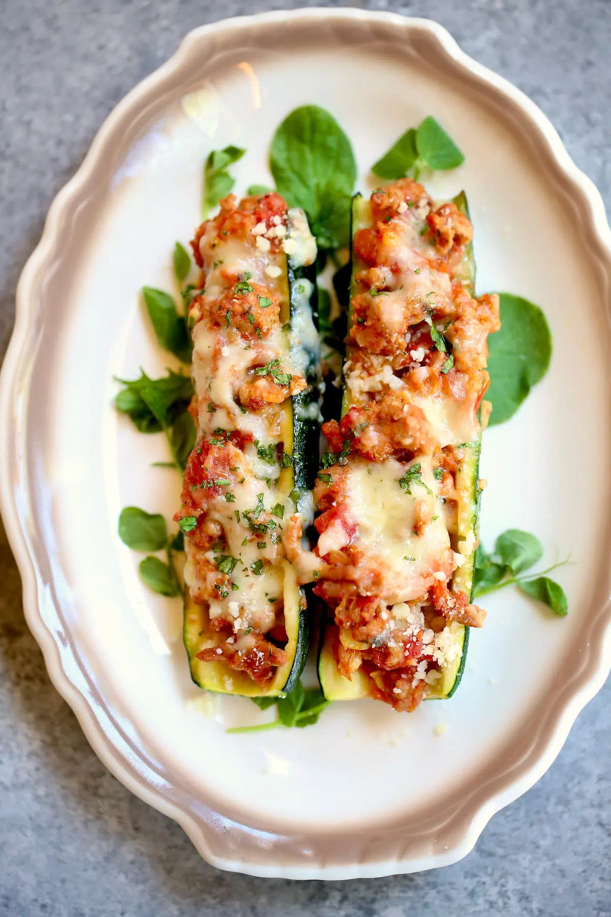 Ground beef mozzarella zucchini boats on white plate.