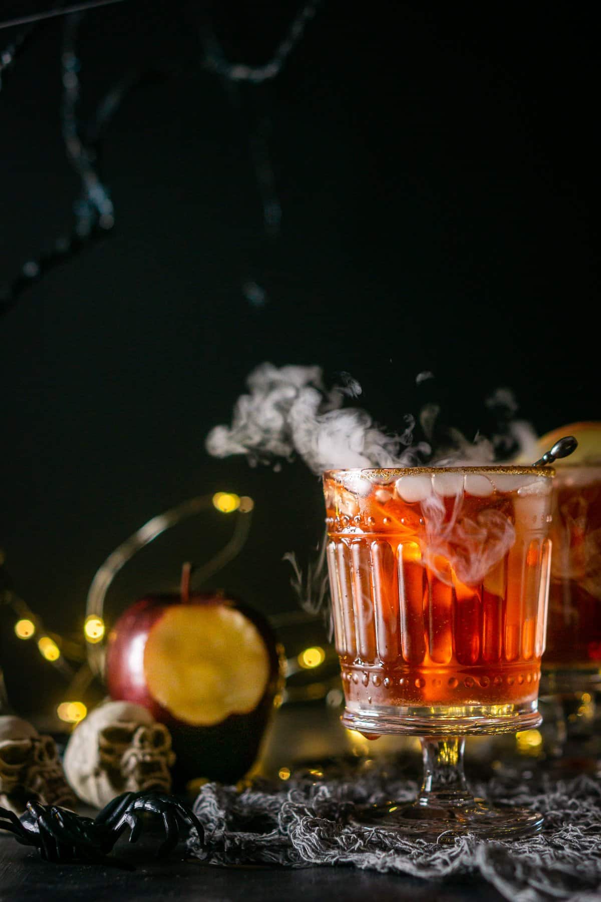 Bubbling, smoky cocktail in a glass with apples, skull and spider props in the background.