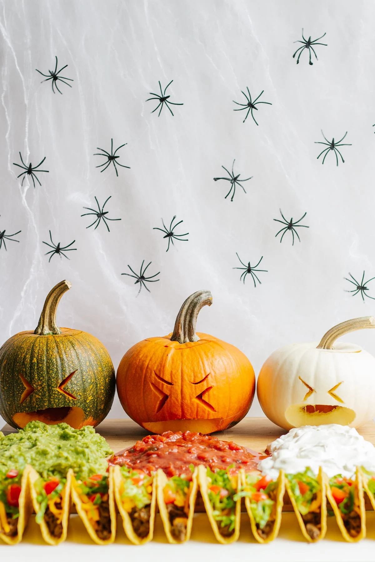 Tacos, guacamole, salsa, sour cream, with festive carved Pumpkins and spiders in the background.