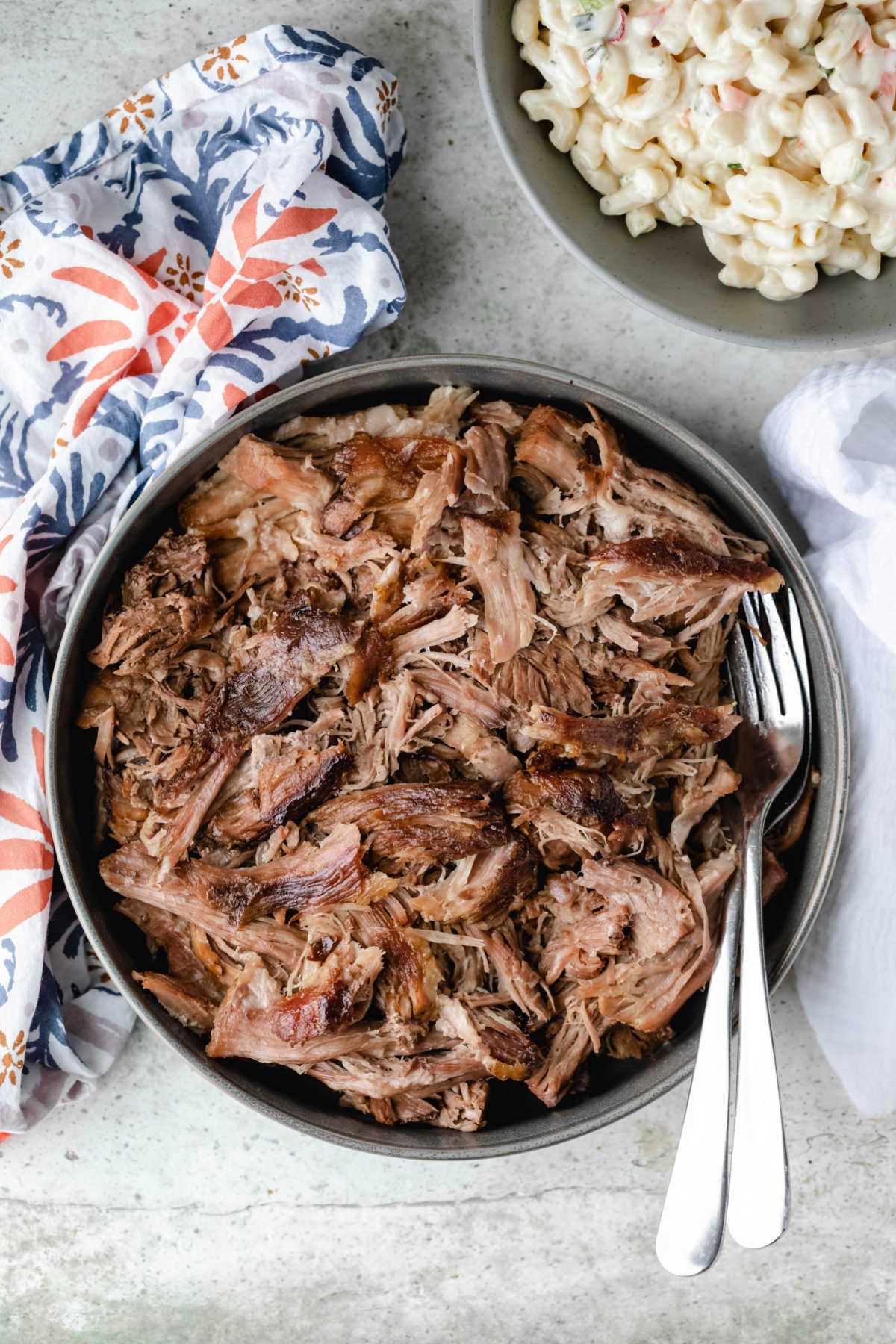 Slow cooker kalua pork in a gray bowl with forks and multicolored napkins in background.