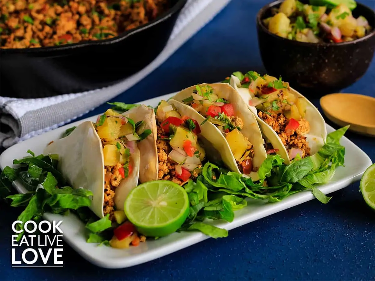 Tofu tacos with pineapple salsa on a white serving plate with blue background.