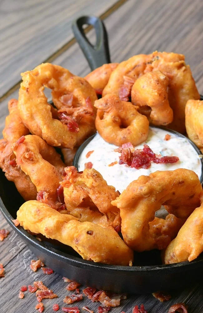 Bacon onion rings in a cast iron pan with bacon ranch in the center on a wooden background.