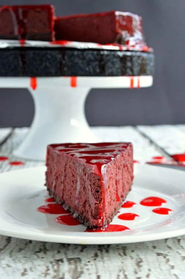 Red cheesecake slice with whole cake in background.