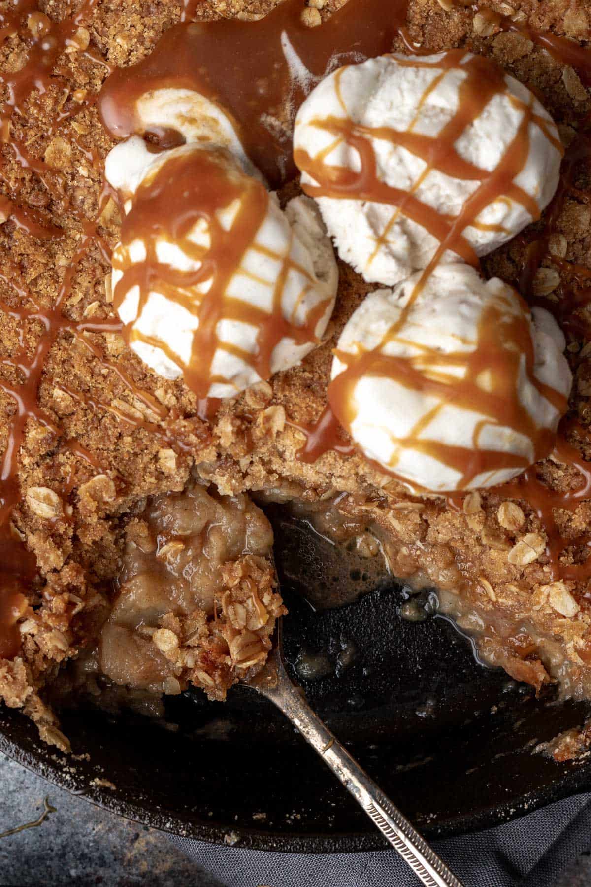 Apple crisp dessert with ice cream and caramel sauce in a cast iron pan.