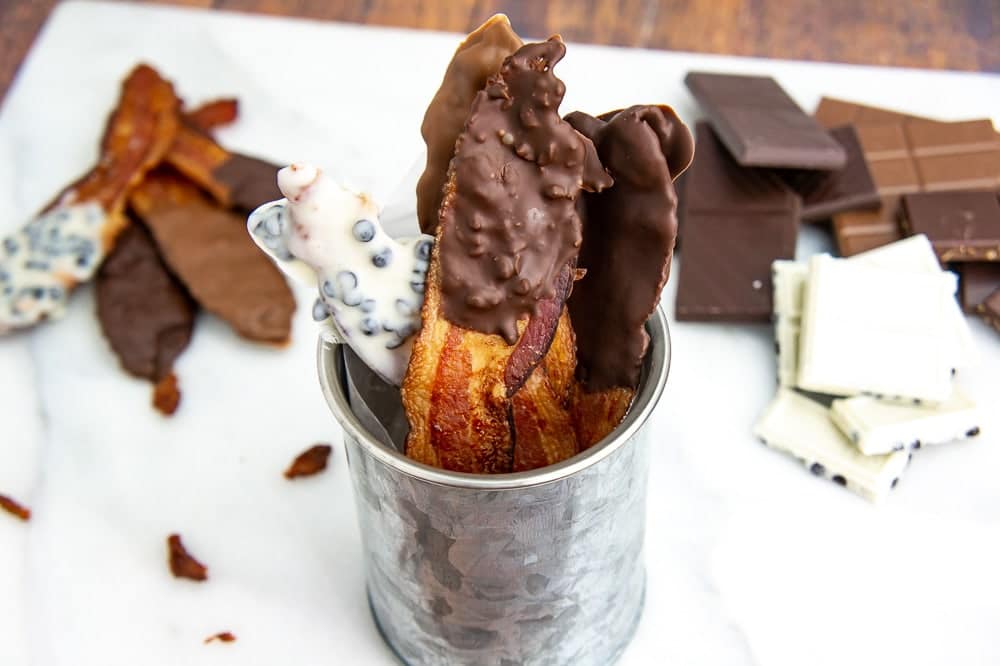 Chocolate covered bacon in a metal can with chocolate bars in the background.