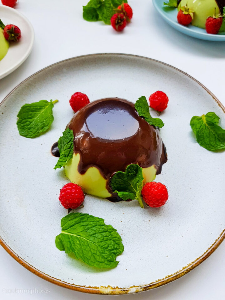 Chocolate pandan panna cotta on a white plate with raspberries and leaves.