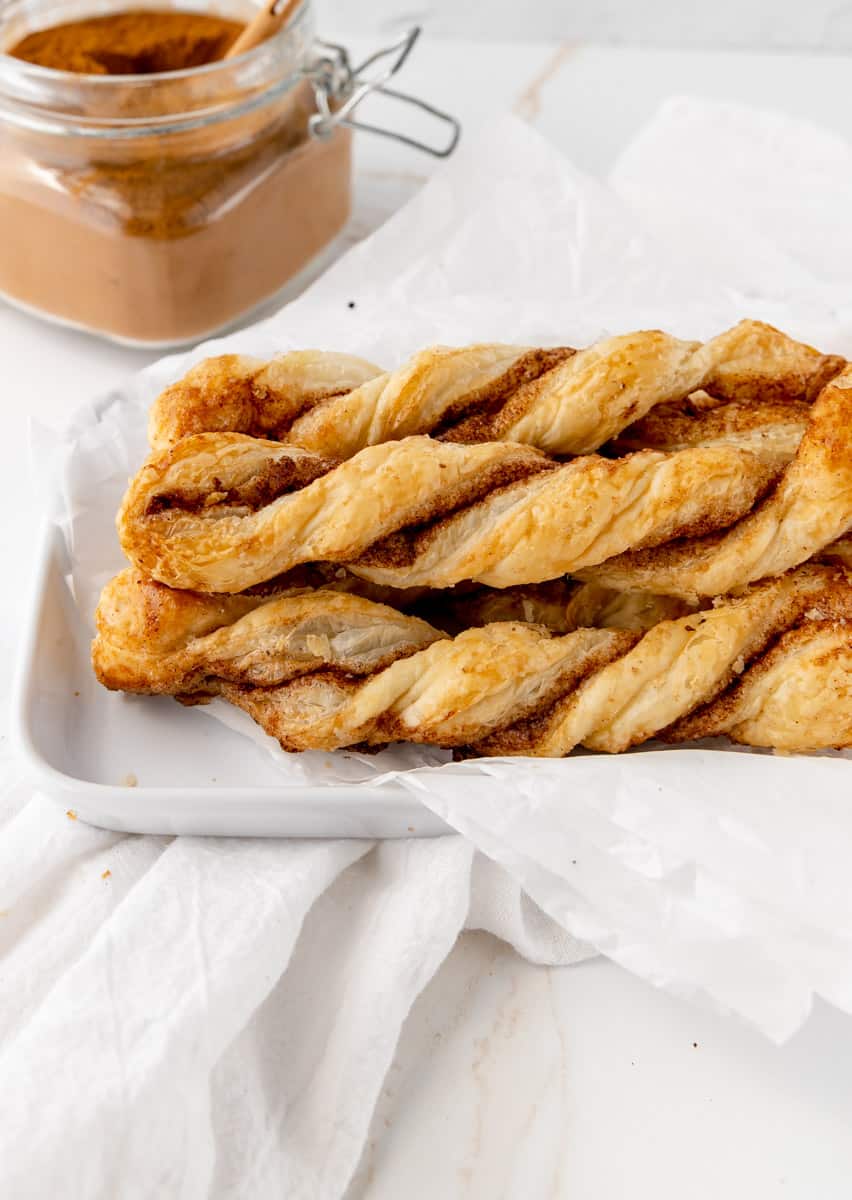 Puff pastry cinnamon twist on parchment paper in a tray with more cinnamon in the background.