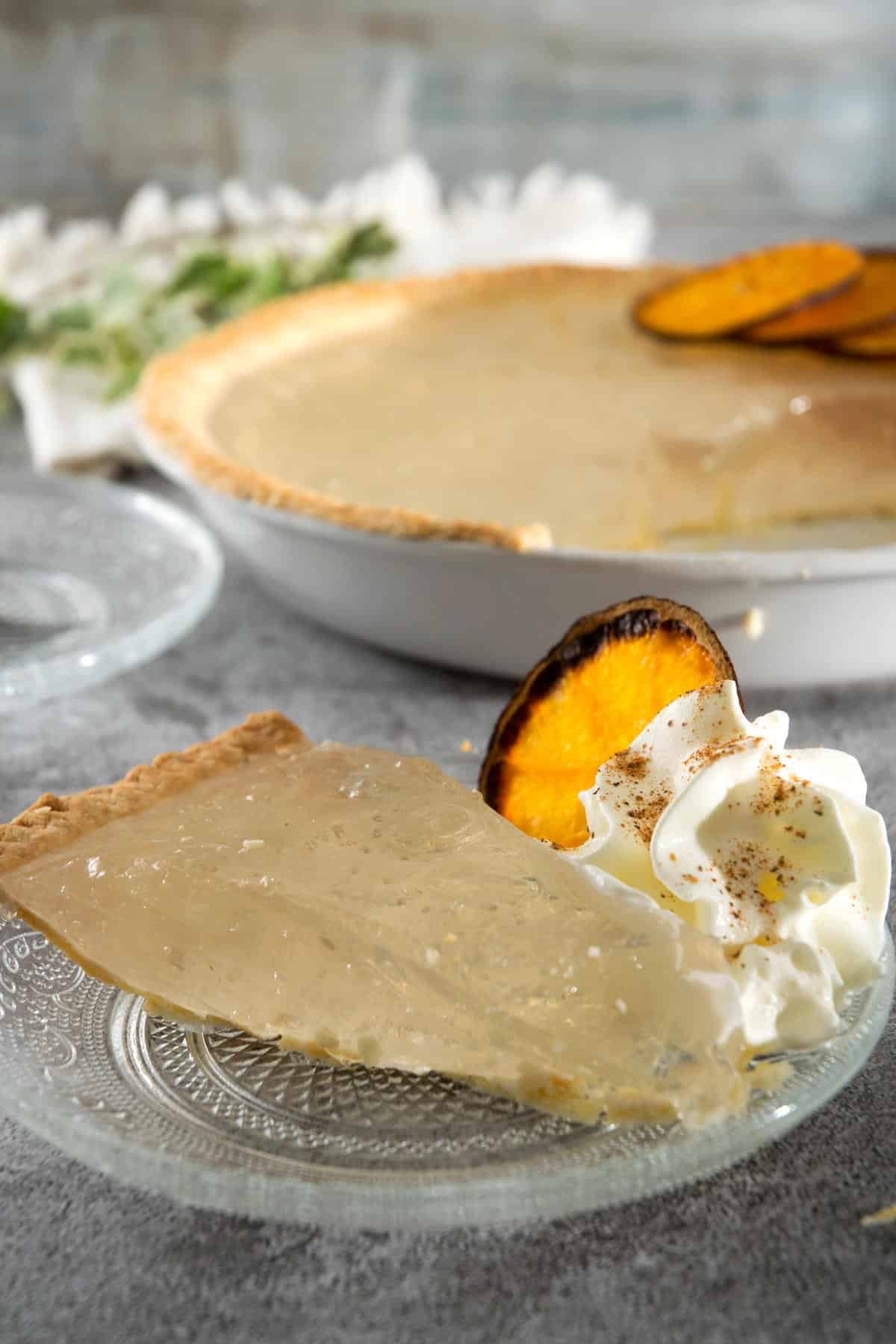 Clear pumpkin pie slice with an orange slice and whipped cream on a clear plate.