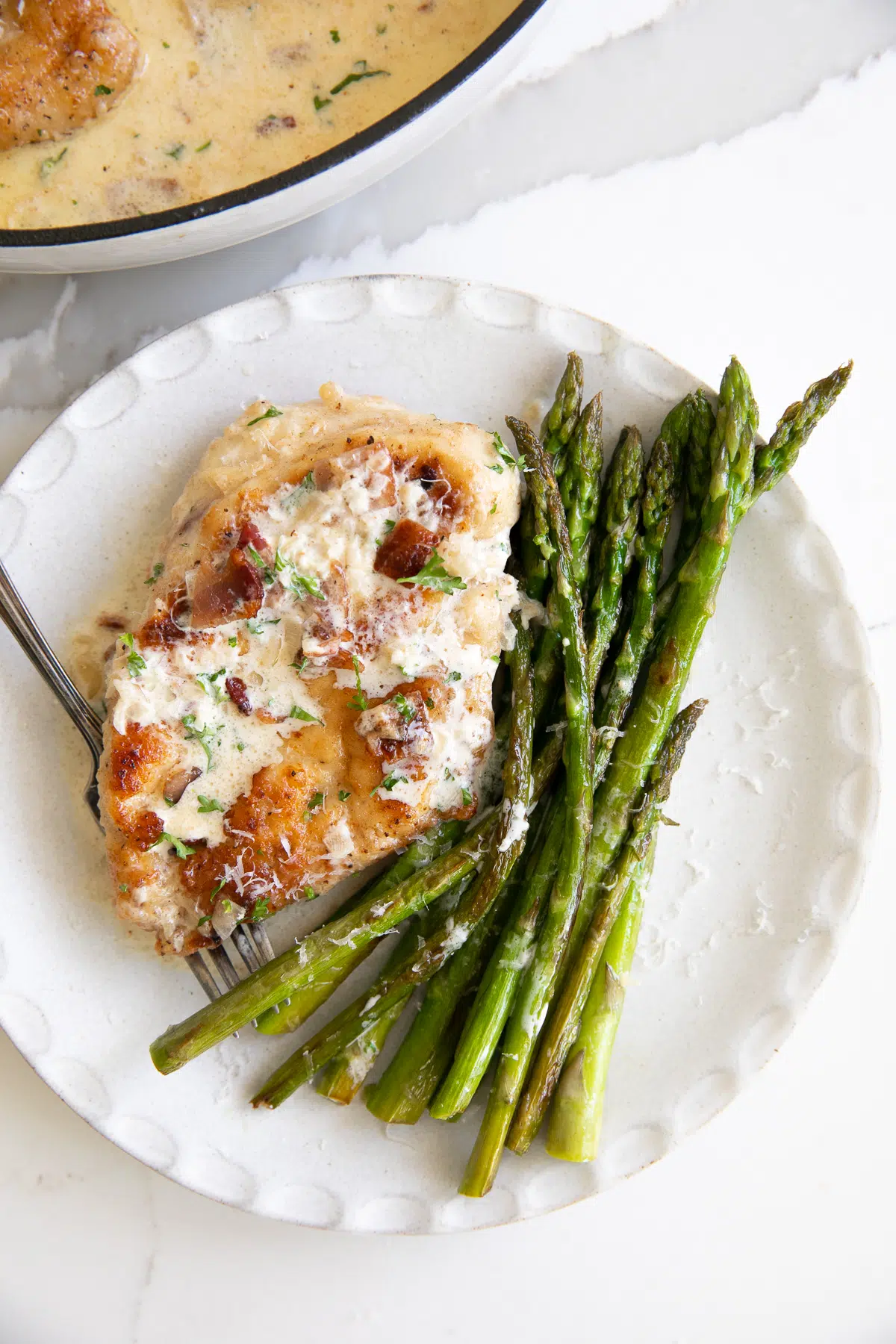 Creamy bacon chicken recipe with asparagus on a white plate.