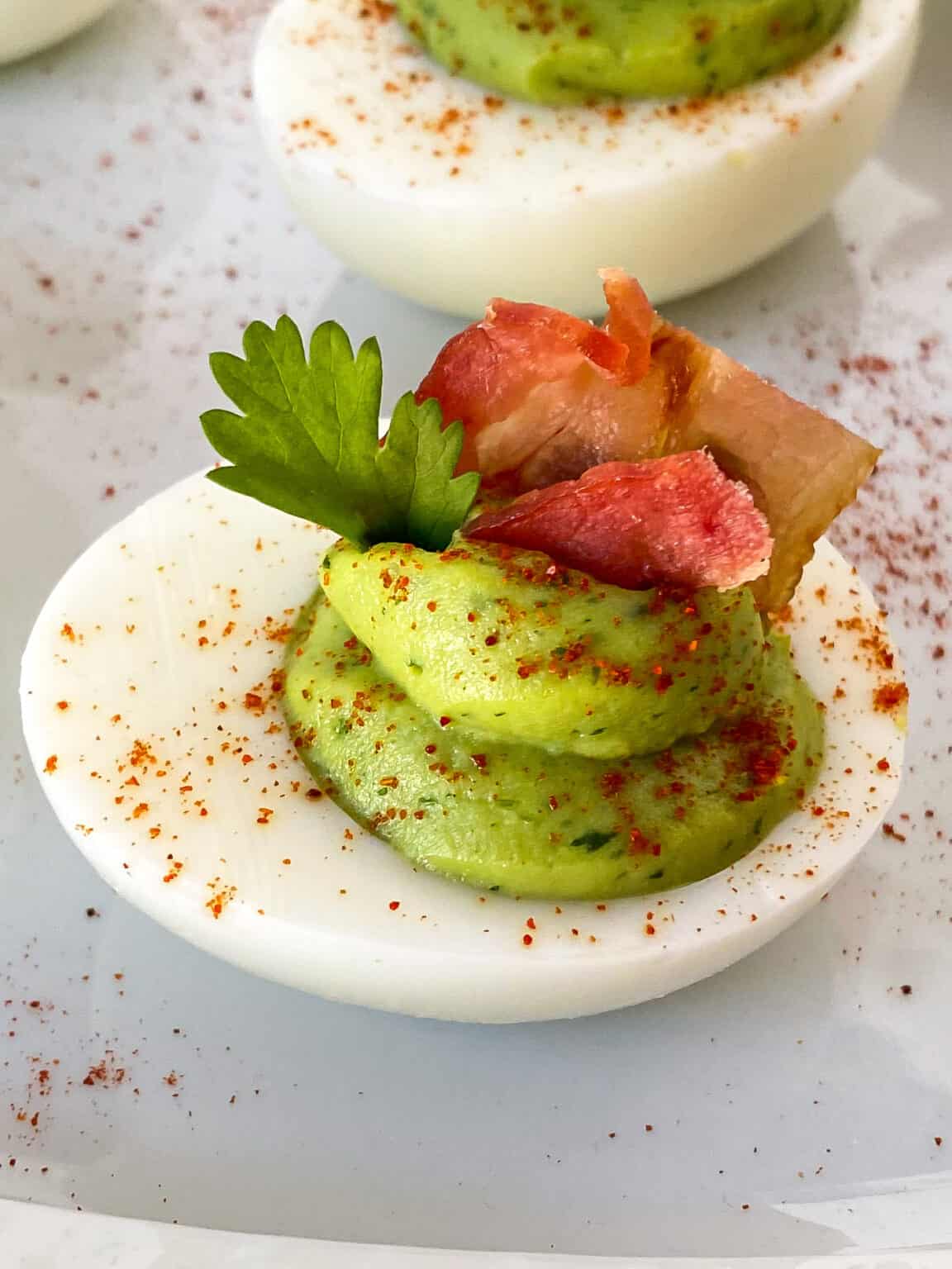 Bacon avocado deviled eggs on a white plate.