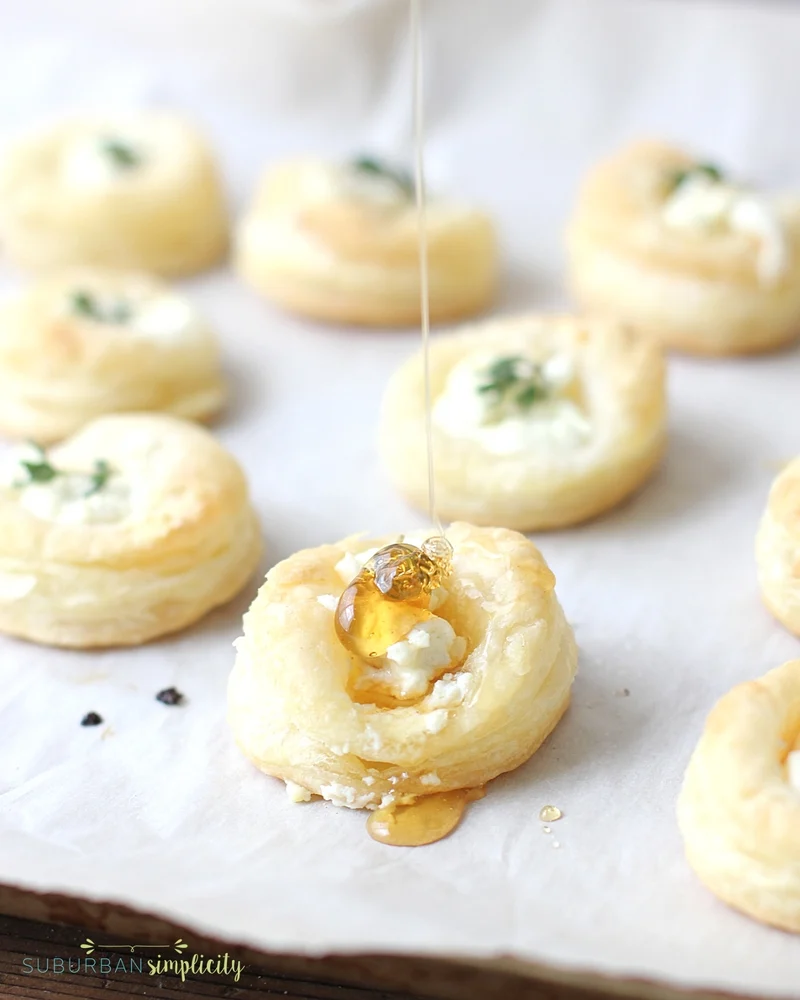 Goat cheese puff pastry bites with honey being drizzled on one.