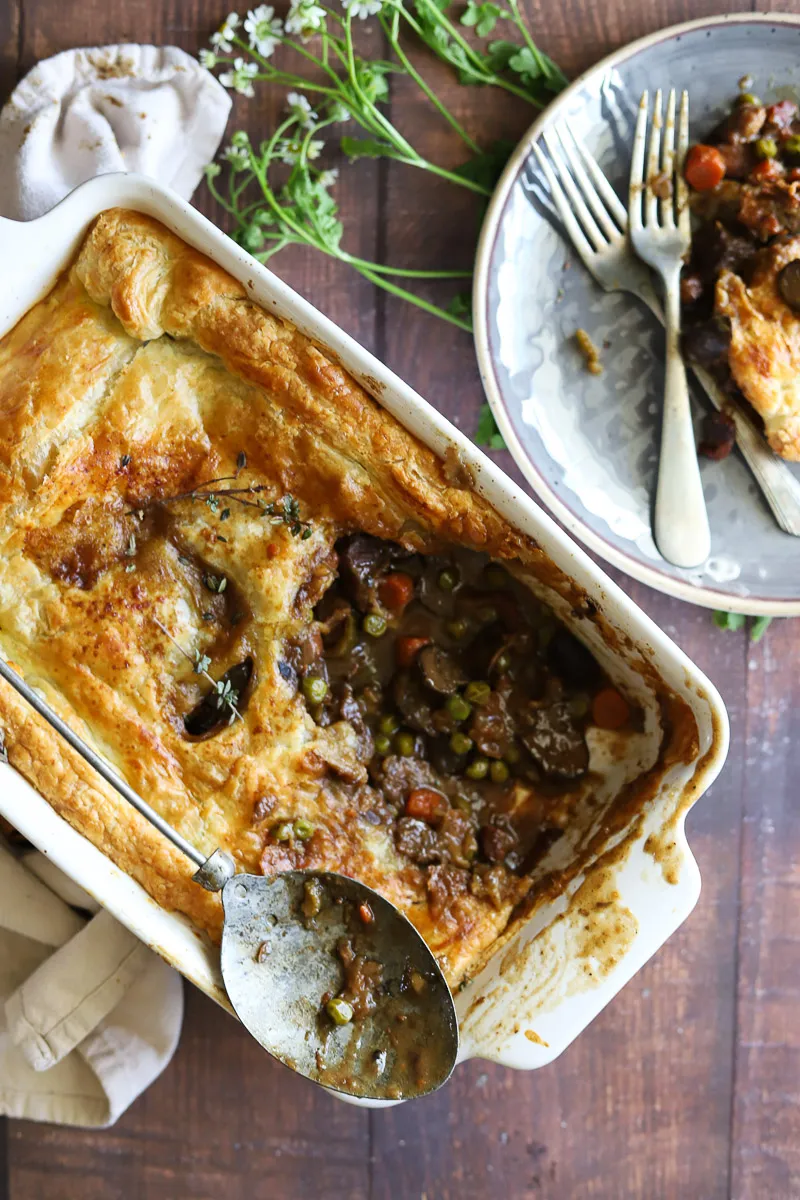 Puff pastry meat pie in baking pan with a serving on a plate with forks.