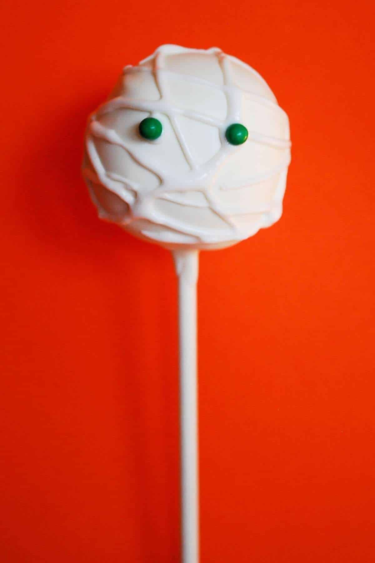 Mummy styled cake pops with green eyeballs and an orange backdrop.