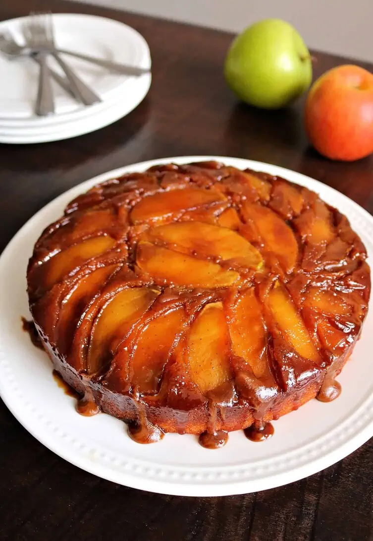 Caramel apple upside down cake on white plate with apples in the background.