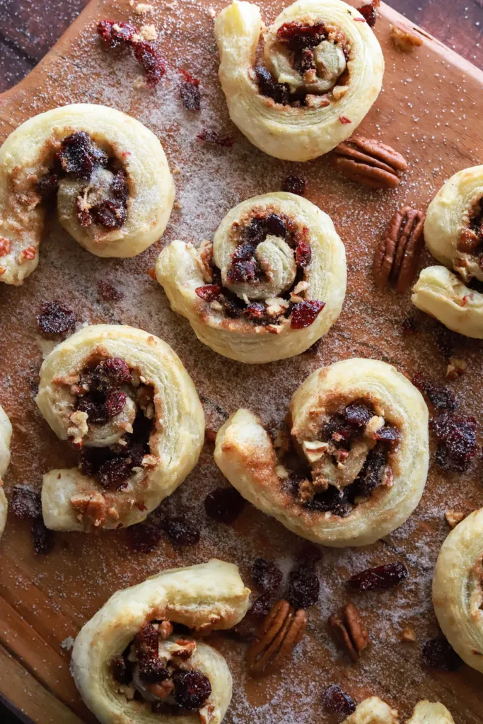 Cinnamon cranberry puff pastry pinwheels with sugar and nuts on a wooden background.
