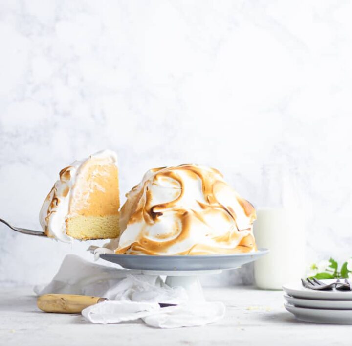 Pumpkin baked Alaska with slice removed on platter with plates in the background.