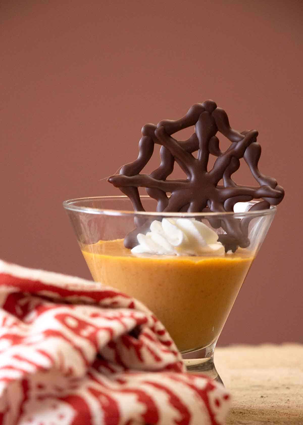 Pumpkin pudding in a glass with chocolate spider web and whipped cream.