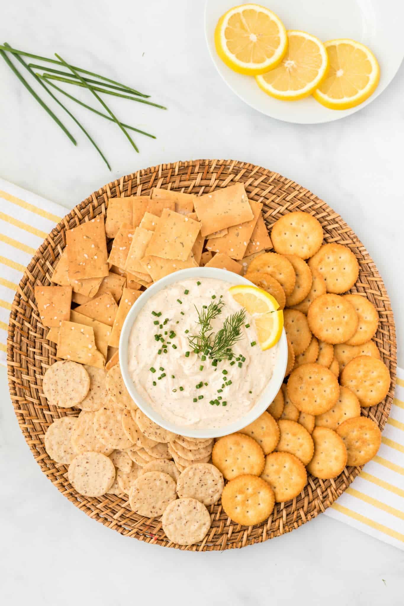 Smoked salmon dip with crackers on a woven platter with lemon on plate in background.