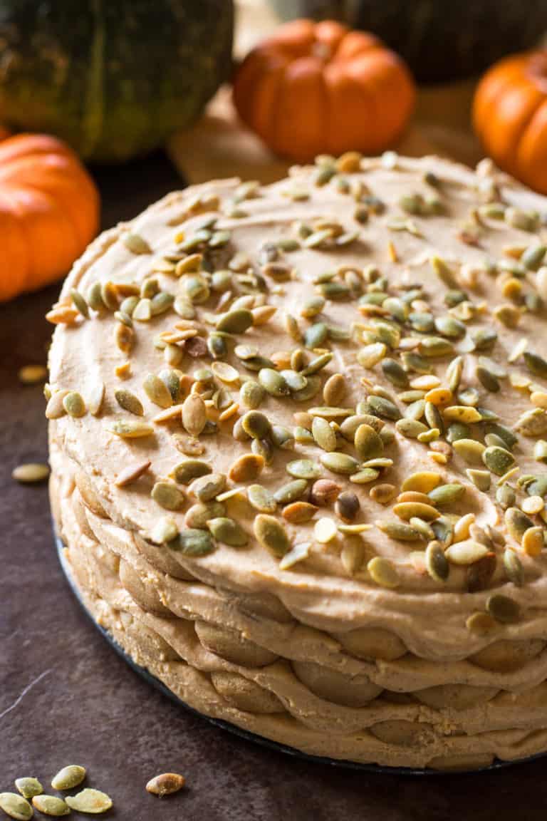 Pumpkin tiramisu formed into a cake with pistachios on top with pumpkins in the background. 