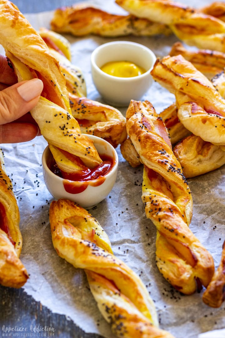 Bunch of bacon puff pastry twist with ketchup and mustard on a parchment paper.