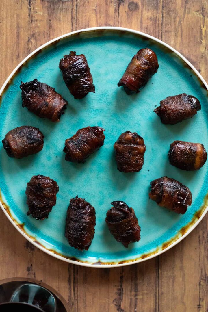 Bacon wrapped dates on a blue plate.