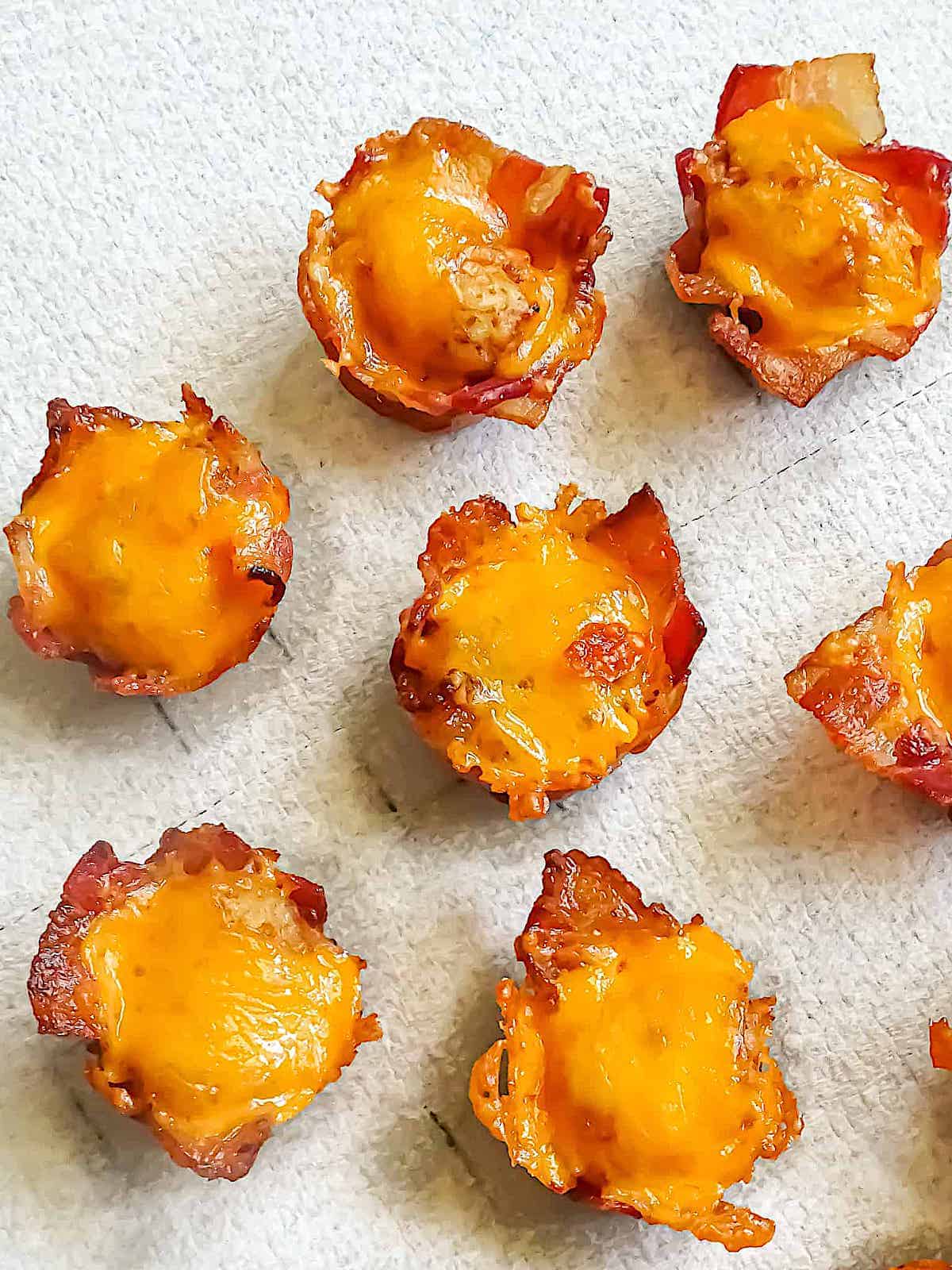 Bacon cups filled with tater tots and cheese on white background.